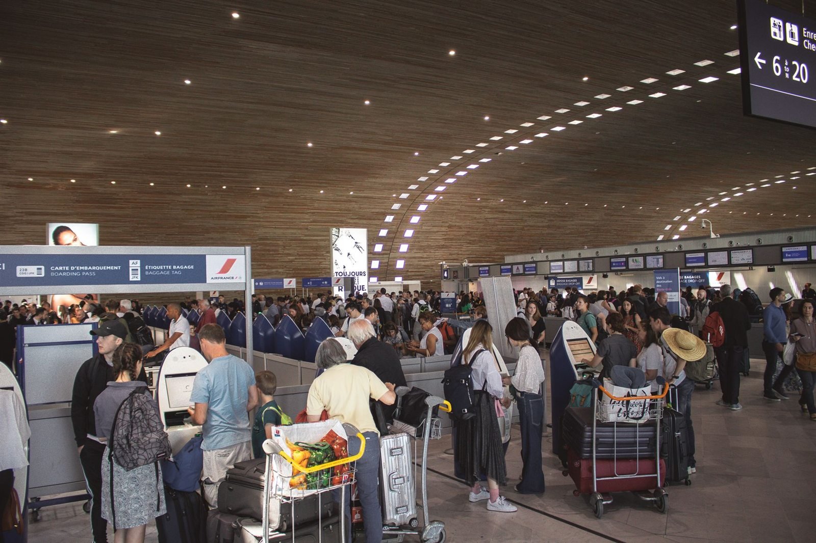 Passengers with luggage trolleys queuing at airline desks in a busy airport terminal
